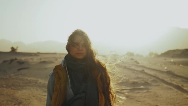 Retrato de una mujer bonita al atardecer. Mujer joven y feliz de pie en el viento contra un paisaje desértico puesta de sol, cámara lenta . — Vídeos de Stock