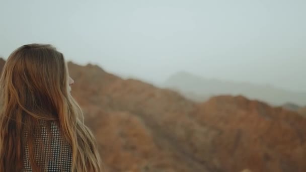 Mujer rubia joven en vestido largo camina en la cima de la montaña. Paisaje de montaña con puesta de sol, cámara lenta, 4k — Vídeos de Stock