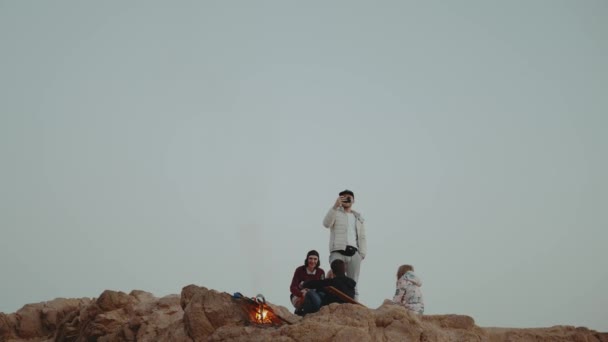 Grupo de amigos relajándose en la cima de una montaña al atardecer, sentados cerca de la hoguera, disfrutando de su tiempo - amistad, juventud, cámara lenta, 4k — Vídeos de Stock