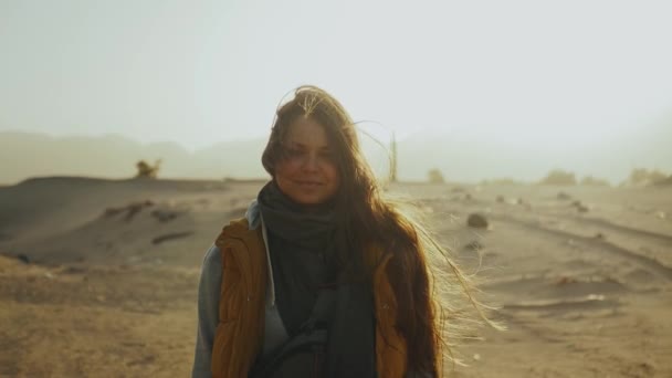 Portrét krásné ženy při západu slunce. Šťastná mladá žena stojící ve větru proti pouštní krajině západu slunce, zpomalený pohyb. — Stock video