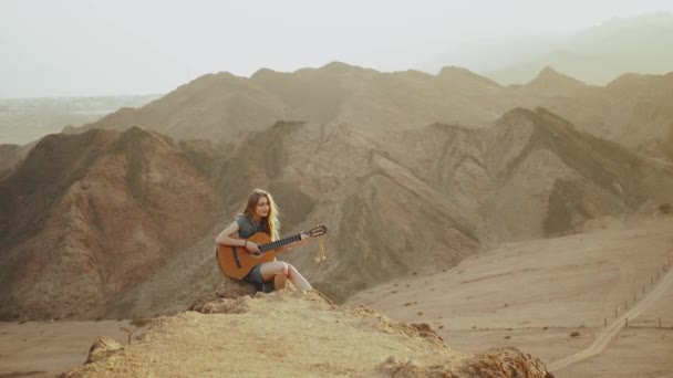 在沙漠风景、沙漠山脉背景、慢动作、 4k中弹奏吉他和唱歌的女性 — 图库视频影像