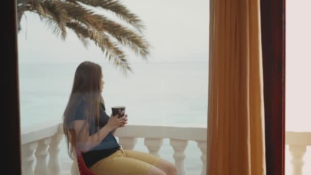 Donna sola sta bevendo caffè o tè al mattino sul balcone con vista mare blu, punto di vista dalla finestra, video rapido, rallentatore, 4k — Video Stock