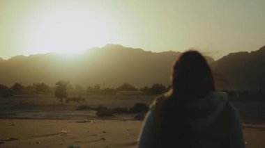 Gün batımında çölde yürüyen güzel genç bir kadının silueti. Çölde giden kadın, kum tepeleri, yakın çekim, yavaş çekim, 4k