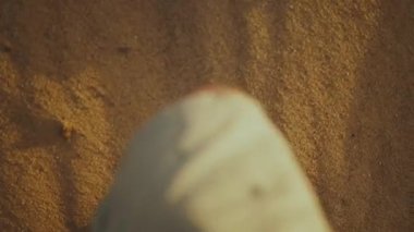 Şortlu erkek bacakları gün batımında kumda yürüyor, ağır çekimde..