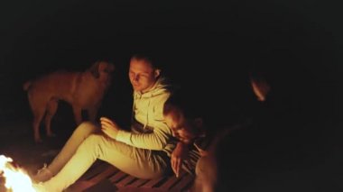 Bir grup arkadaş, gece deniz kenarındaki kumsalda kamp ateşinin yanında eğleniyor. Hızlı video, ağır çekim, 4k