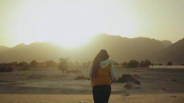 Kız sahilde yürüyüp Horizon 'u araştırıyor. Kadının sırtından kumsal ve mavi deniz manzarası, yavaş çekim, 4k