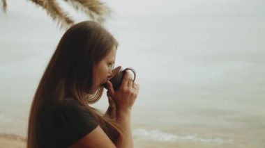 Sabahları balkonda tek başına kahve ya da çay içen bir kadın. Mavi deniz manzaralı, pencereden bakan, hızlı çekim, ağır çekim, 4k