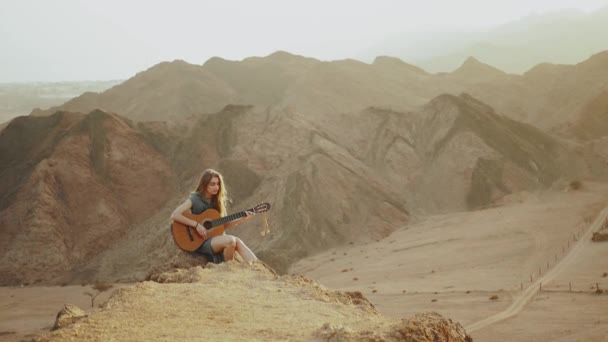 Kvinna spelar gitarr och sjunger i ökenlandskap, öken berg bakgrund, slow motion, 4k — Stockvideo