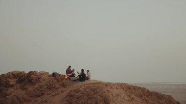 Bir grup arkadaş gün batımında dağın tepesinde, şenlik ateşinin yanında oturup eğleniyorlar - arkadaşlık, gençlik, ağır çekim, 4k 
