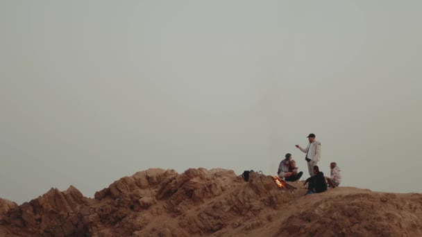 Grupo de amigos relaxando no topo de uma montanha ao pôr-do-sol, sentados perto da fogueira, desfrutando de seu tempo amizade, juventude, câmera lenta, 4k — Vídeo de Stock