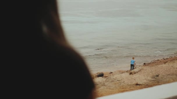 Samotna kobieta pije rano kawę lub herbatę na balkonie z niebieskim widokiem na morze, dzieci bawią się na plaży w pobliżu morza, szybki film, zwolnione tempo, 4k — Wideo stockowe