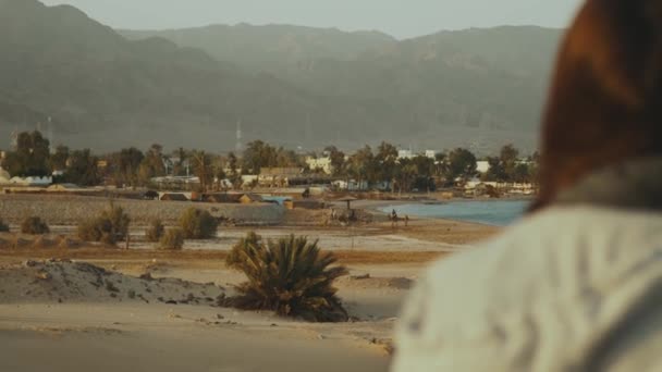 Utsikt över sandstrand och blått hav från baksidan av honan. Flicka stanna på stranden och titta in i Horizon, slow motion. — Stockvideo