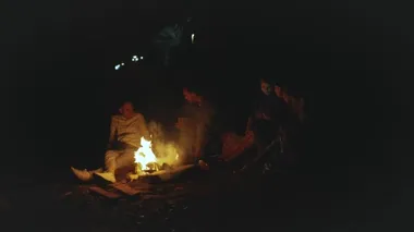 Bir grup arkadaş, gece deniz kenarındaki kumsalda kamp ateşinin yanında eğleniyor. Hızlı video, ağır çekim, 4k