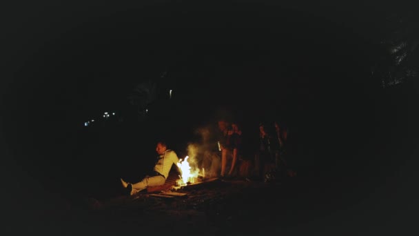Grupo de amigos se divertindo perto da fogueira na praia perto do mar à noite, vídeo rápido, câmera lenta, 4k — Vídeo de Stock