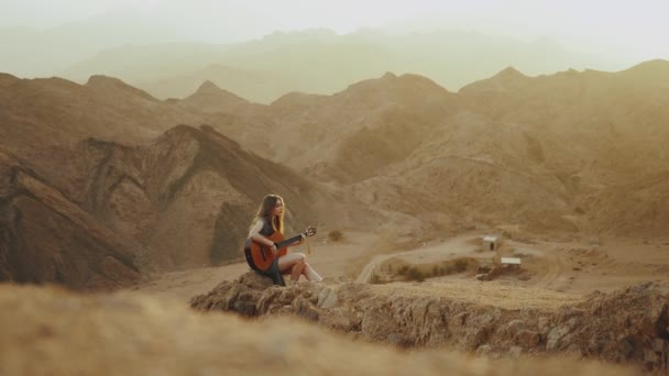 Kvinna spelar gitarr och sjunger i ökenlandskap, öken berg bakgrund, slow motion, 4k — Stockvideo