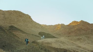 Bir grup turist sıcak çölde kaya kanyonu boyunca yürür, turistler fotoğraf çeker ve eğlenirler. Çöl dağları arka planı, Mısır, Sina, yavaş çekim, 4k