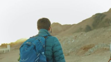Bir grup turist sıcak çölde kaya kanyonu boyunca yürür, turistler fotoğraf çeker ve eğlenirler. Çöl dağları arka planı, Mısır, Sina, yavaş çekim, 4k