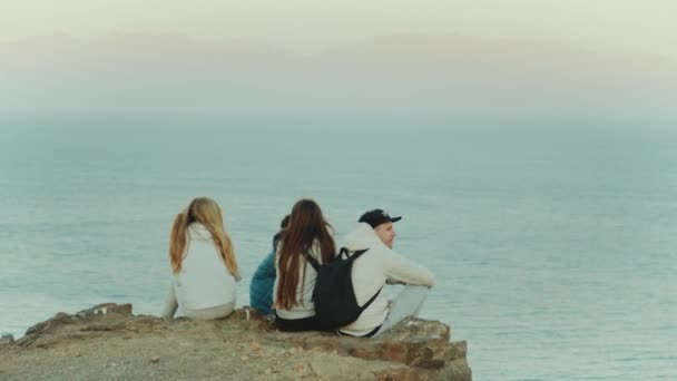 Grupo de amigos relaxando no topo de uma montanha ao pôr do sol e desfrutando de vista mar - amizade, juventude, câmera lenta, 4k — Vídeo de Stock