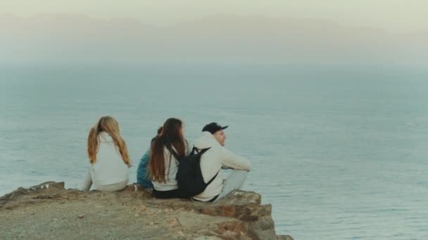 Grupo de amigos relaxando no topo de uma montanha ao pôr do sol e desfrutando de vista mar - amizade, juventude, câmera lenta, 4k — Vídeo de Stock