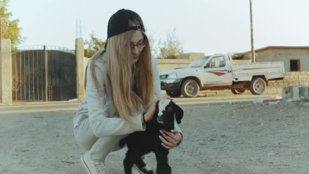 Mulher jovem loira bonita acaricia o menino de cabra preto e branco em Dahab, Egito, Sinai, câmera lenta, 4k — Vídeo de Stock