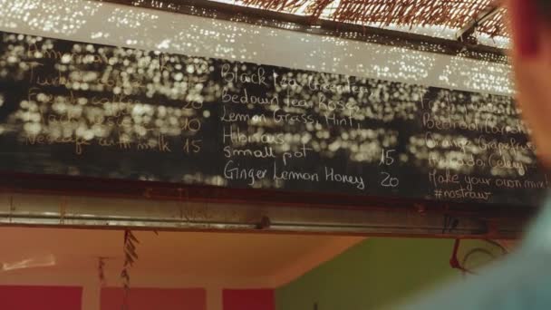 Zpět pohled na zákazníka muž podívat se na menu na zdi ve vegetariánském obchodě vybrat nápoj, čerstvé šťávy v menu v Dahab shop, Egypt, zpomalení, 4k — Stock video