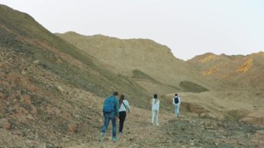 Bir grup turist sıcak çölde kaya kanyonu boyunca yürür, turistler fotoğraf çeker ve eğlenirler. Çöl dağları arka planı, Mısır, Sina, yavaş çekim, 4k