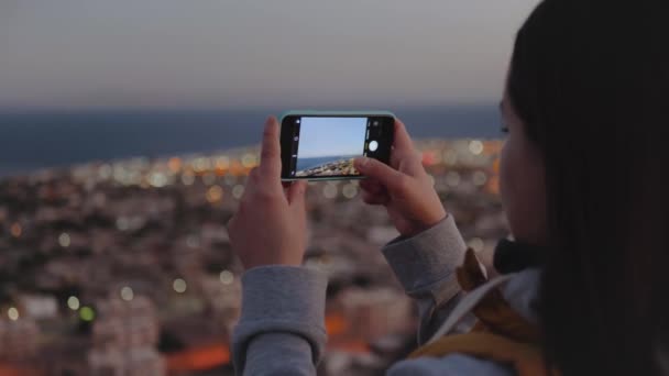 Mulher tirar fotos do mar por smartphone à noite. Mulher ficar no topo da montanha e olhando para o horizonte, câmera lenta, 4k — Vídeo de Stock