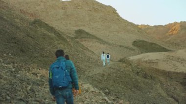 Bir grup turist sıcak çölde kaya kanyonu boyunca yürür, turistler fotoğraf çeker ve eğlenirler. Çöl dağları arka planı, Mısır, Sina, yavaş çekim, 4k