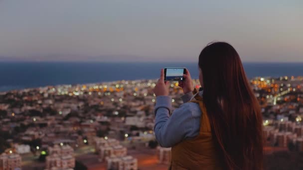 女性は夕方にスマートフォンで海の写真を撮る。女性は山の上に滞在し、地平線、スローモーション、 4kに見て — ストック動画