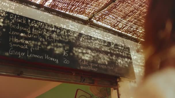 Vista posteriore della donna cliente guardare il menu a parete nel negozio vegetariano scegliere bevanda, succhi di frutta freschi nel menu nel negozio Dahab, Egitto, rallentatore, 4k — Video Stock