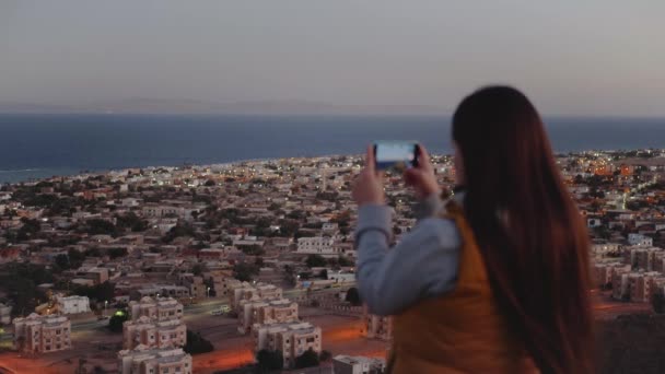 Akşamları kadın akıllı telefondan denizin fotoğrafını çeker. Kadın dağın tepesinde durur ve Horizon 'a bakar, ağır çekimde, 4k — Stok video