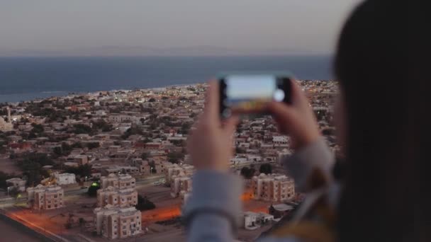 Вечером женщина фотографирует море со смартфона. Женщина оставаться на вершине горы и глядя в Горизонт, замедленное движение, 4k — стоковое видео