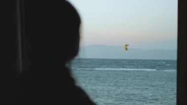 Kadın şarap içiyor ve bak insanlar Dahab Mısır 'da temiz suda nasıl sörf yapıyor. Arka planda dağlar olan mavi denizi keşfetmek ve insanlar uçurtma sörfü, yavaş çekim, 4k