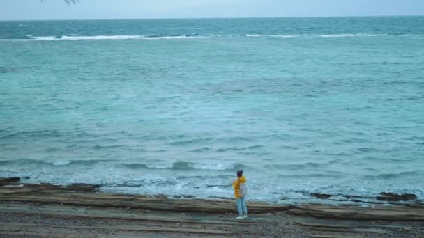 Mujer bonita caminando y tomando fotos en la playa costera pedregosa cerca del mar, las olas se rompen en la orilla, Egipto Sinaí montaña en el fondo, cámara lenta, 4k — Vídeos de Stock