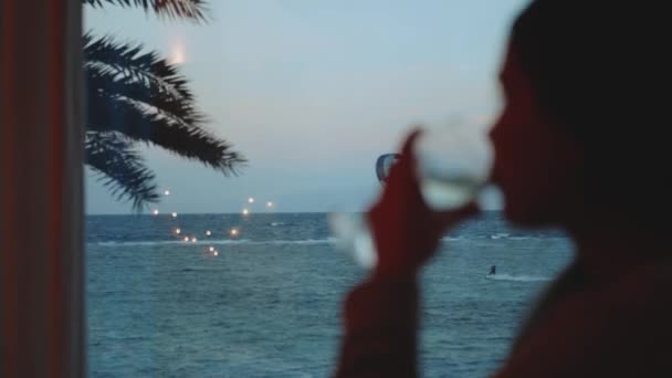 Kadın şarap içiyor ve bak insanlar Dahab Mısır 'da temiz suda nasıl sörf yapıyor. Arka planda dağlar olan mavi denizi keşfetmek ve insanlar uçurtma sörfü, yavaş çekim, 4k — Stok video