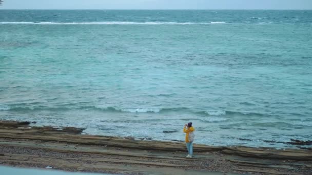 Jolie femme marchant et prenant des photos sur la plage de rivage pierreux près de la mer, les vagues se brisent sur le rivage, Egypte Sinaï montagne sur le fond, ralenti, 4k — Video