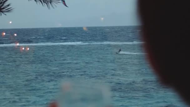 Femme boire du vin et regarder comment les gens cerf-volant surf dans une belle eau claire à Dahab Egypte. Explorer la mer bleue avec des montagnes en arrière-plan et les gens kite surf, ralenti, 4k — Video