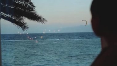 Kadın şarap içiyor ve bak insanlar Dahab Mısır 'da temiz suda nasıl sörf yapıyor. Arka planda dağlar olan mavi denizi keşfetmek ve insanlar uçurtma sörfü, yavaş çekim, 4k