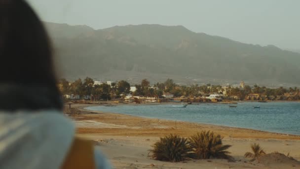 Vista de praia de areia e mar azul de costas de fêmea. Menina ficar na praia e olhando para o horizonte, câmera lenta . — Vídeo de Stock
