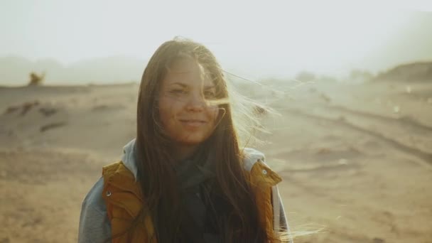 Retrato de una mujer bonita al atardecer. Mujer joven y feliz de pie en el viento contra un paisaje desértico puesta de sol, cámara lenta . — Vídeos de Stock