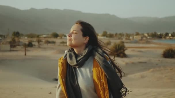 Kobieta z długimi włosami chodzić po pustyni, morze i góry na tle, zwolnione tempo. — Wideo stockowe