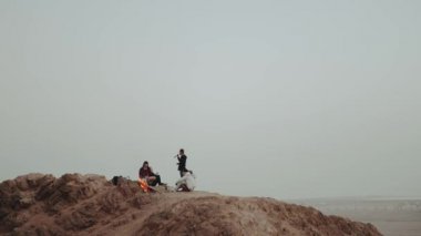 Gün batımında bir dağın tepesinde dinlenen bir grup insan, şenlik ateşinin yanında oturmuş, eğleniyorlar - arkadaşlık, gençlik, ağır çekim, tam kapasite