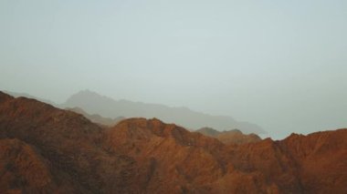 Mısır 'ın çöl dağlarında inanılmaz bir gün batımı. Ufkun altındaki güneşten gelen ışıklar dağların üstündeki gökyüzünü aydınlatır. Silüet. Yavaş çekim, tam ışık.