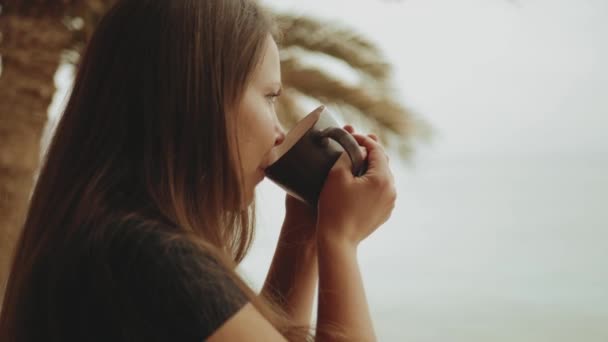 Donna sola sta bevendo caffè o tè al mattino sul balcone con vista mare blu, punto di vista dalla finestra, video rapido, rallentatore, full hd — Video Stock