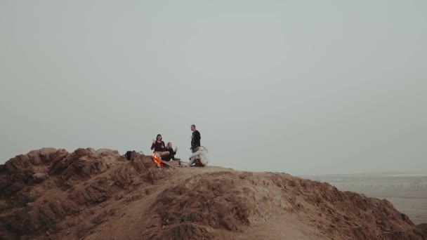 Skupina lidí relaxuje na vrcholu hory při západu slunce, sedí blízko táboráku, užívají si svůj čas - přátelství, mládež, zpomalení, full hd — Stock video
