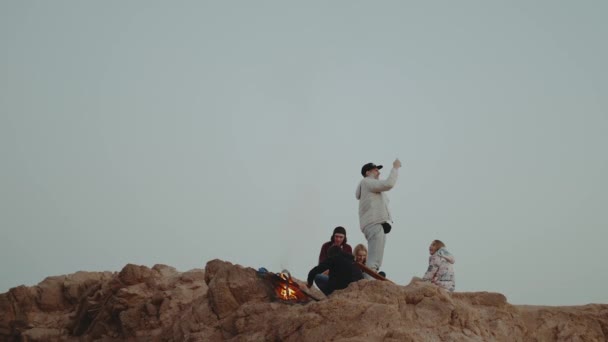 Groupe de personnes se relaxant au sommet d'une montagne au coucher du soleil, assis près d'un feu de joie, profitant de leur temps amitié, jeunesse, ralenti, pleine HD — Video