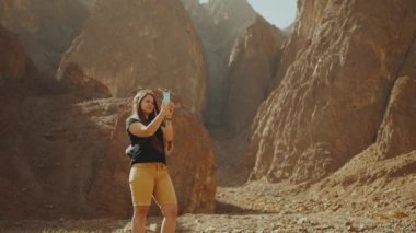 Turist kadın kayalık kanyon boyunca yürür ve sıcak çölde fotoğraf çeker. Çöl kanyonu arka planı, Mısır, Sina, yavaş çekim, full hd