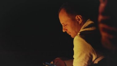 Bir grup arkadaş, gece deniz kenarındaki kumsalda kamp ateşinin yanında eğleniyor. Hızlı video, yavaş çekim, tam yol ileri.
