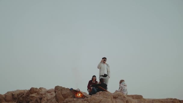 Группа людей отдыхает на вершине горы на закате, сидит у костра, наслаждаясь своим временем - дружба, молодежь, замедленное движение, полный hd — стоковое видео