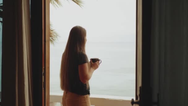 Donna sola sta bevendo caffè o tè al mattino sul balcone con vista mare blu, punto di vista dalla finestra, video rapido, rallentatore, full hd — Video Stock